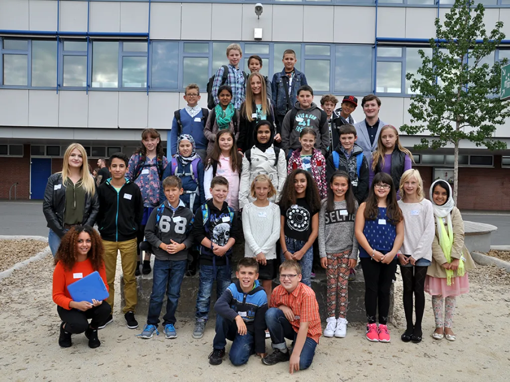 Klassenfoto einer neuen fünften Klasse mit Lehrkräften am Sandkasten.